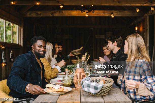 portrait of smiling man enjoying with male and female friends during social gathering - nordic food stock-fotos und bilder