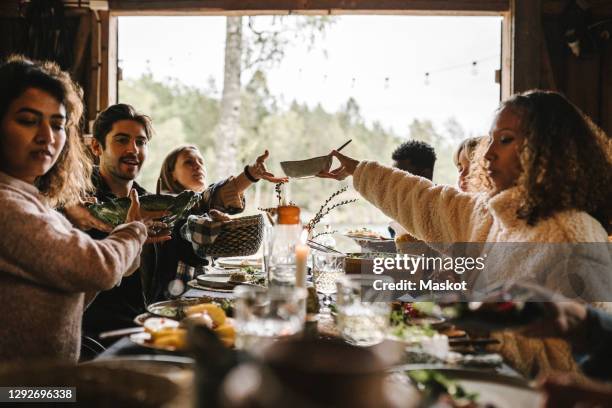 female passing food bowl to friend over table during social event - dinertje stockfoto's en -beelden