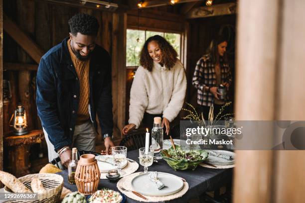 smiling man and woman arranging plates over dining table - white dinner jacket stock pictures, royalty-free photos & images