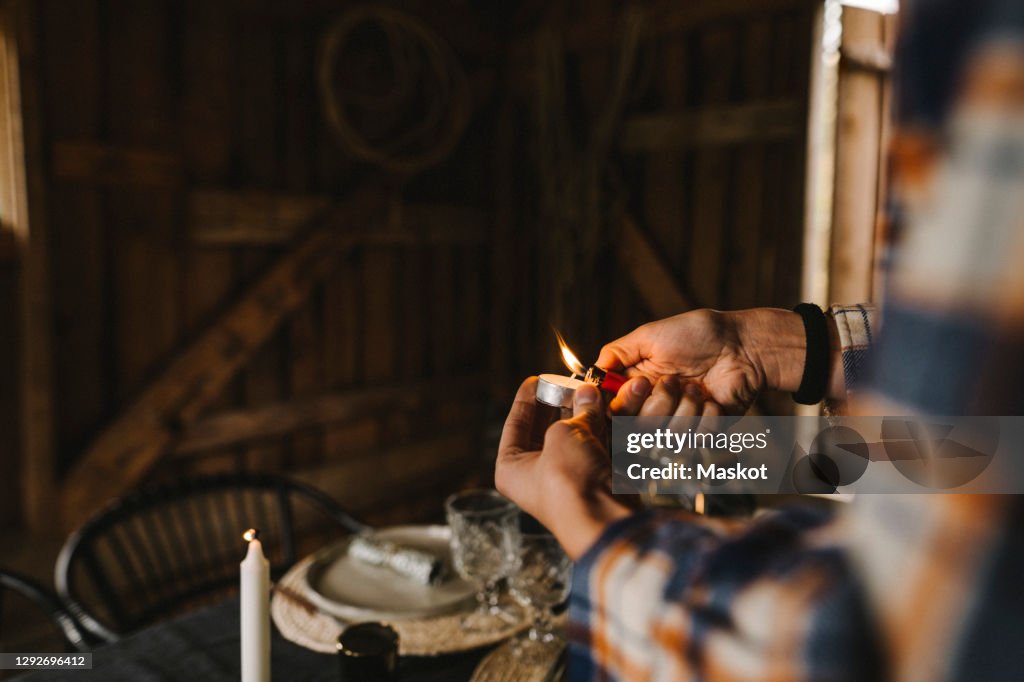Cropped image of woman igniting candle by dining table during social gathering