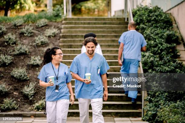 smiling female and male colleagues with disposable cup moving down on staircase - hospital exterior stock pictures, royalty-free photos & images