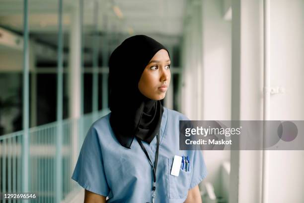 contemplating female nurse looking through window while standing in hospital corridor - thinking of you card - fotografias e filmes do acervo