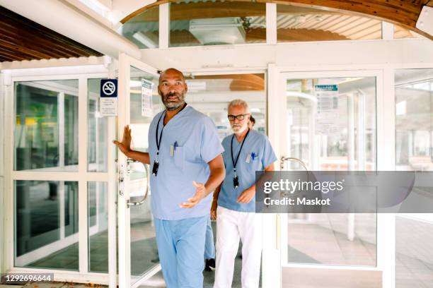 mature nurse talking to senior colleague while holding hospital door - entering hospital stock pictures, royalty-free photos & images