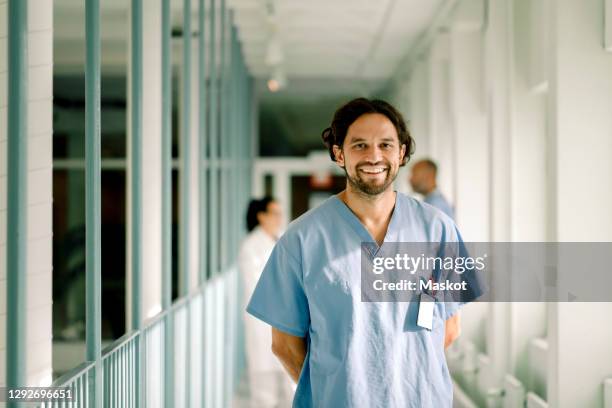 portrait of smiling male nurse standing in hospital corridor - man in hospital stockfoto's en -beelden