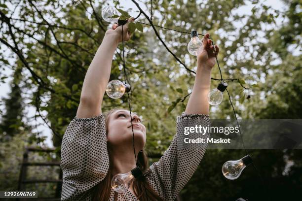 smiling woman hanging lighting equipment in yard during dinner party - decorating photos et images de collection