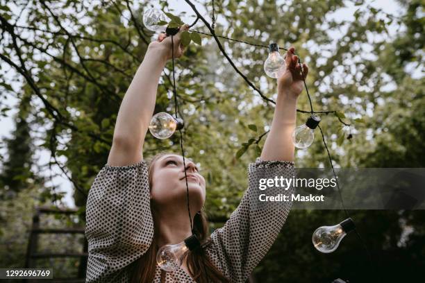 smiling woman hanging lighting equipment in yard during dinner party - string light stock pictures, royalty-free photos & images