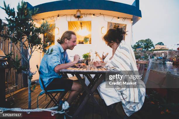 side view of heterosexual couple sitting at table in houseboat during sunset - houseboat stock pictures, royalty-free photos & images