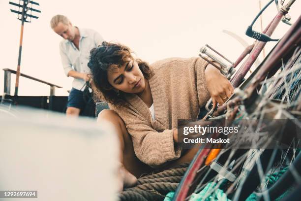 mid adult woman repairing bicycle while boyfriend in background at houseboat - repairing boat stock pictures, royalty-free photos & images