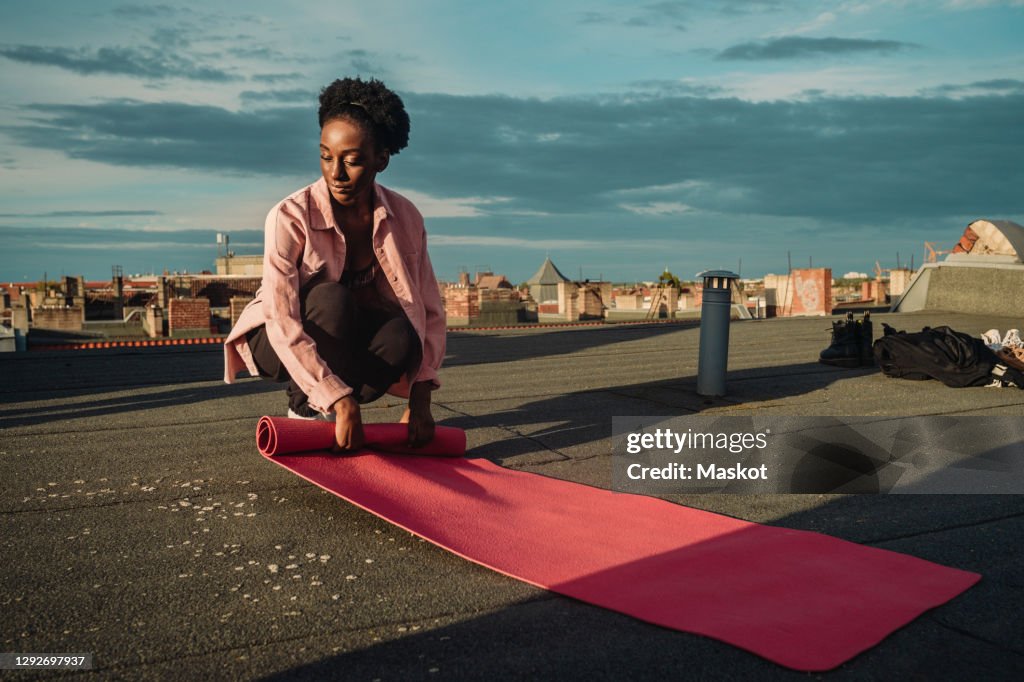 Young female folding exercise mat on rooftop during sunrise