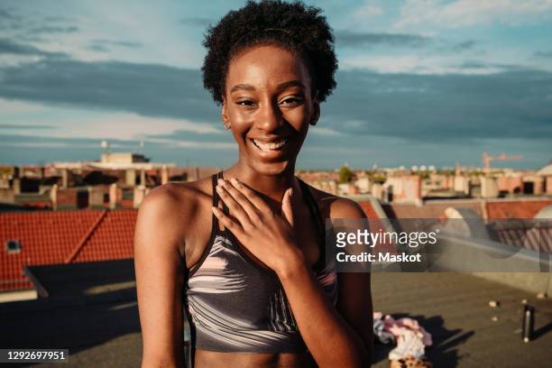 portrait of happy female in sports clothing standing on rooftop during sunrise - sports training stock-fotos und bilder