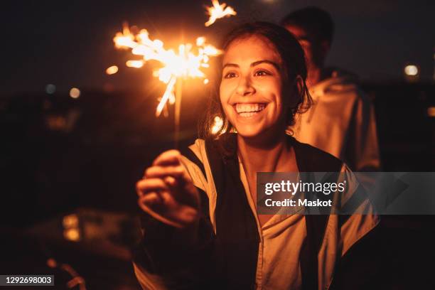 cheerful woman looking at igniting sprinkler on rooftop at night - friends with sparkler fireworks stock pictures, royalty-free photos & images