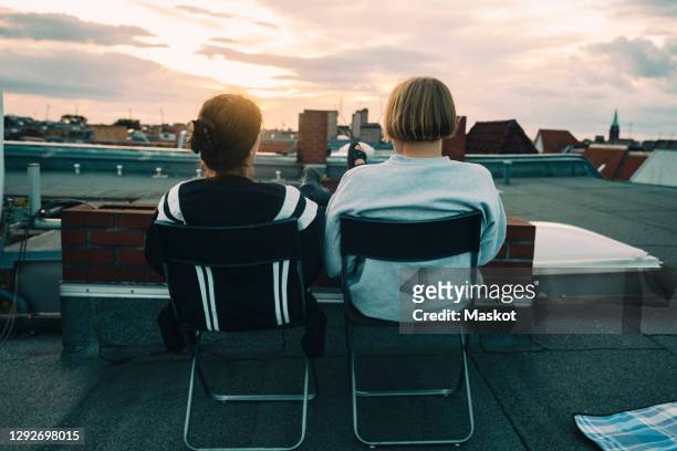 rear view of friends sitting on chair at building terrace - berlin rooftop stockfoto's en -beelden