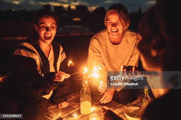 cheerful female with friends igniting sprinkler on building rooftop at night - night picnic stock pictures, royalty-free photos & images