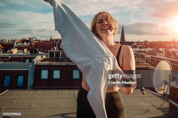 portrait of smiling woman wearing t-shirt on rooftop against dramatic sky - germany womens training stockfoto's en -beelden