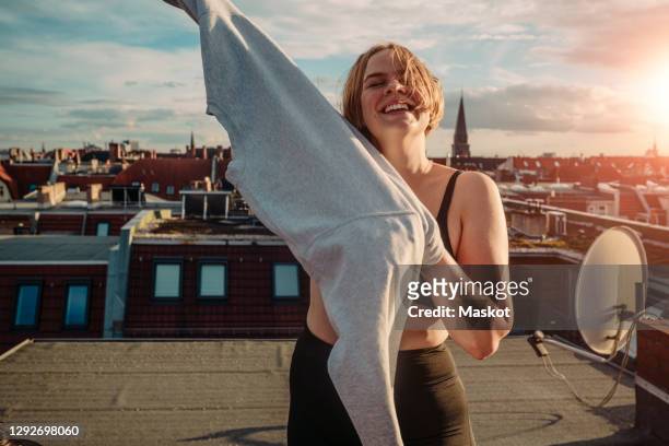 portrait of smiling woman wearing t-shirt on rooftop against dramatic sky - human arm stock pictures, royalty-free photos & images