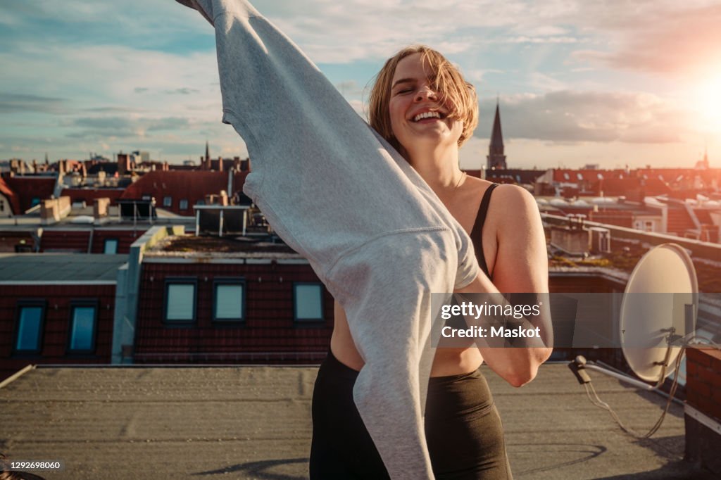 Portrait of smiling woman wearing t-shirt on rooftop against dramatic sky