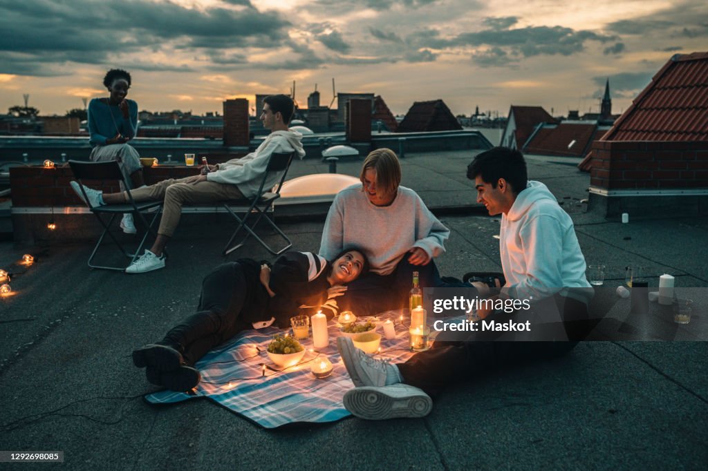 Male and female friends talking on building terrace during sunset