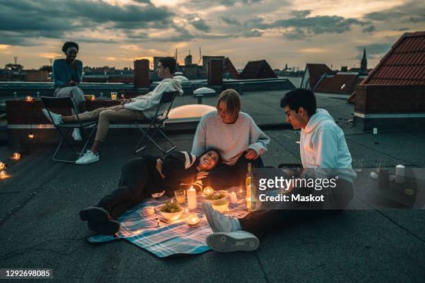 male and female friends talking on building terrace during sunset - evening meal stock pictures, royalty-free photos & images