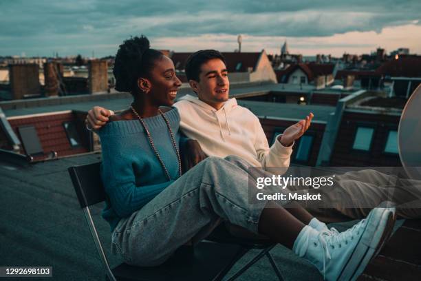 smiling woman and man talking while sitting on building rooftop during sunset - einfaches leben stock-fotos und bilder