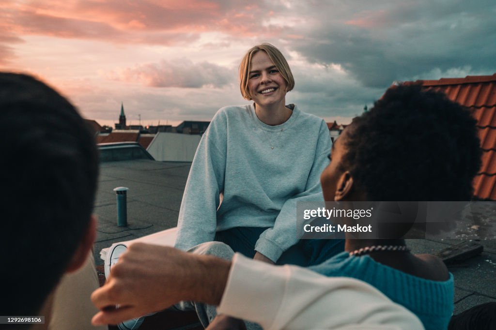 Portrait of smiling female sitting with friends on building terrace during sunset