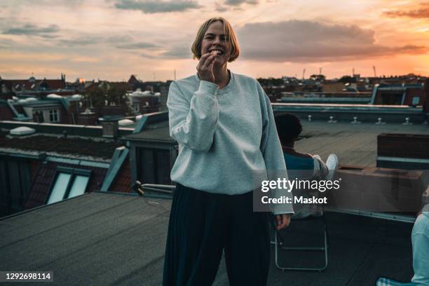 portrait of smiling female with friends enjoying on building terrace during sunset - personas stock-fotos und bilder