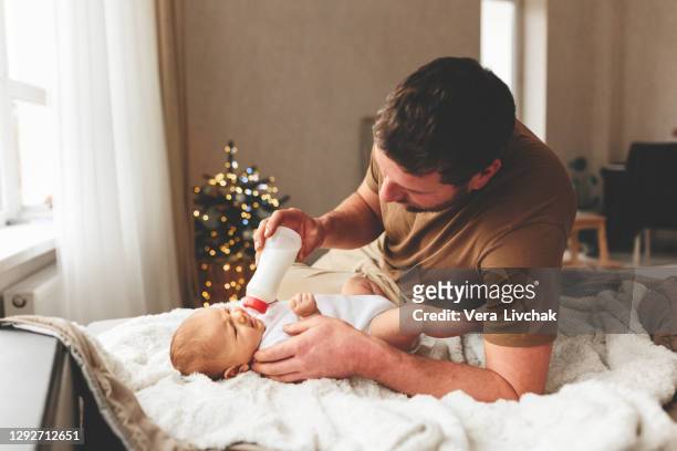 family, parenthood and people concept - father feeding little daughter with baby formula from bottle at home - eltern baby stockfoto's en -beelden
