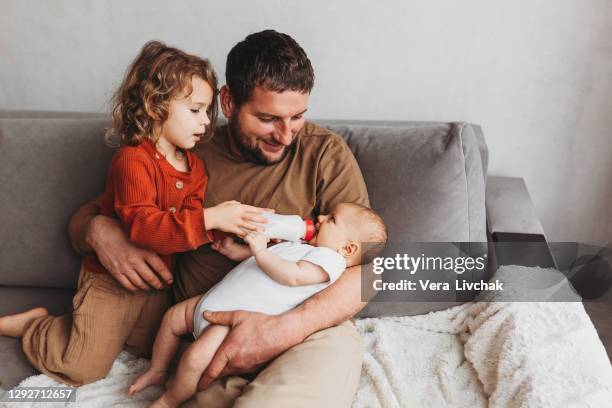 family, parenthood and people concept - father feeding little daughter with baby formula from bottle at home with toddler - eltern baby stockfoto's en -beelden