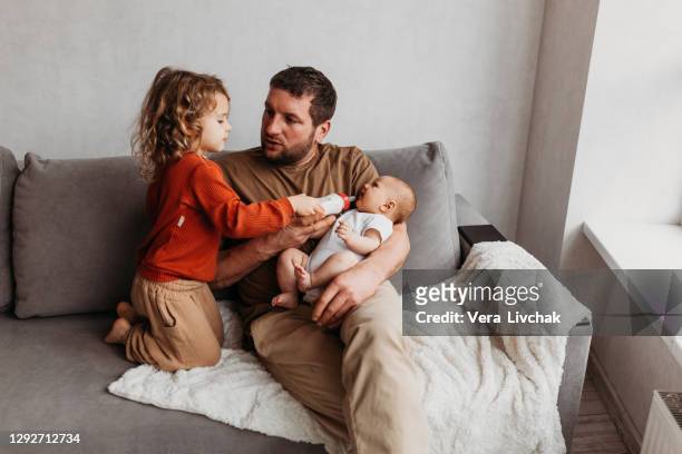 family, parenthood and people concept - father feeding little daughter with baby formula from bottle at home with toddler - eltern stock pictures, royalty-free photos & images