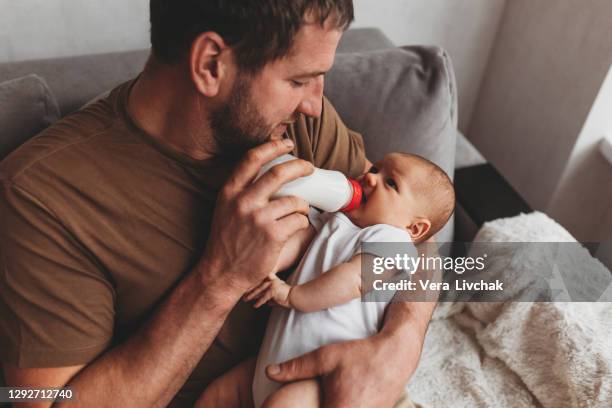 family, parenthood and people concept - father feeding little daughter with baby formula from bottle at home - feeding foto e immagini stock