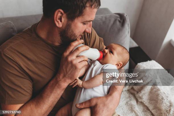 family, parenthood and people concept - father feeding little daughter with baby formula from bottle at home - baby feeding stockfoto's en -beelden