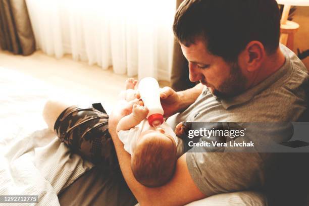 family, parenthood and people concept - father feeding little daughter with baby formula from bottle at home - eltern stock pictures, royalty-free photos & images