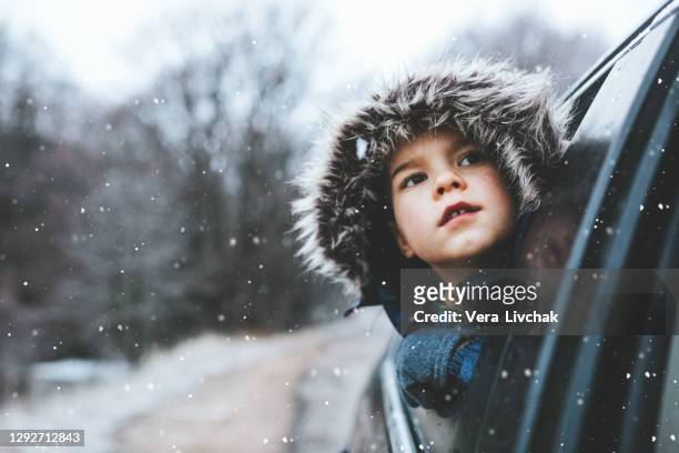 boy on a road trip. the little boy is looking from the car window in winter , opened his mouth and pulled out his tongue, catches snowflakes - christmas driving stockfoto's en -beelden