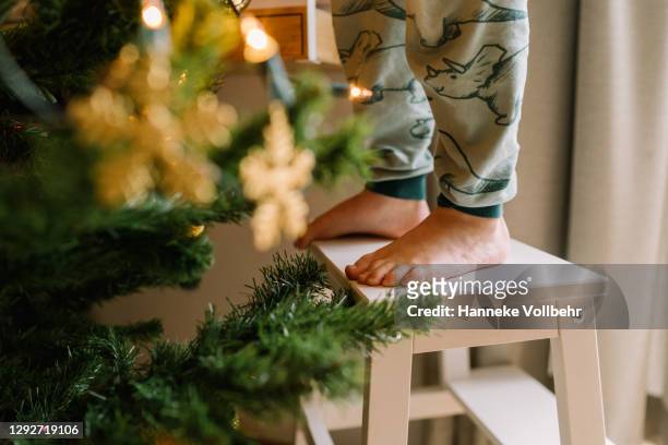 child feet standing on wooden stool to decorate christmas tree - feet christmas stock-fotos und bilder