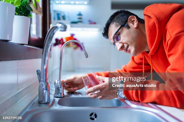 young and worried man is waiting for a last drop of water hangs from a tap with glass under water shortage struck by drought .water shortage and drought crisis with global warming - drought stock pictures, royalty-free photos & images