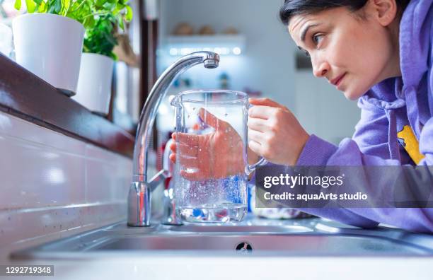 young and worried women is waiting for a last drop of water hangs from a tap with glass under water shortage struck by drought. water shortage and drought crisis with global warming - paisagem árida imagens e fotografias de stock