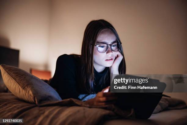 憤怒的看起來少女婦女放鬆在床上的夜晚使用她的數字平板電腦 - suspicion 個照片及圖片檔