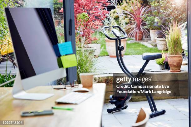 desk in home office and exercise bike - cyclette foto e immagini stock