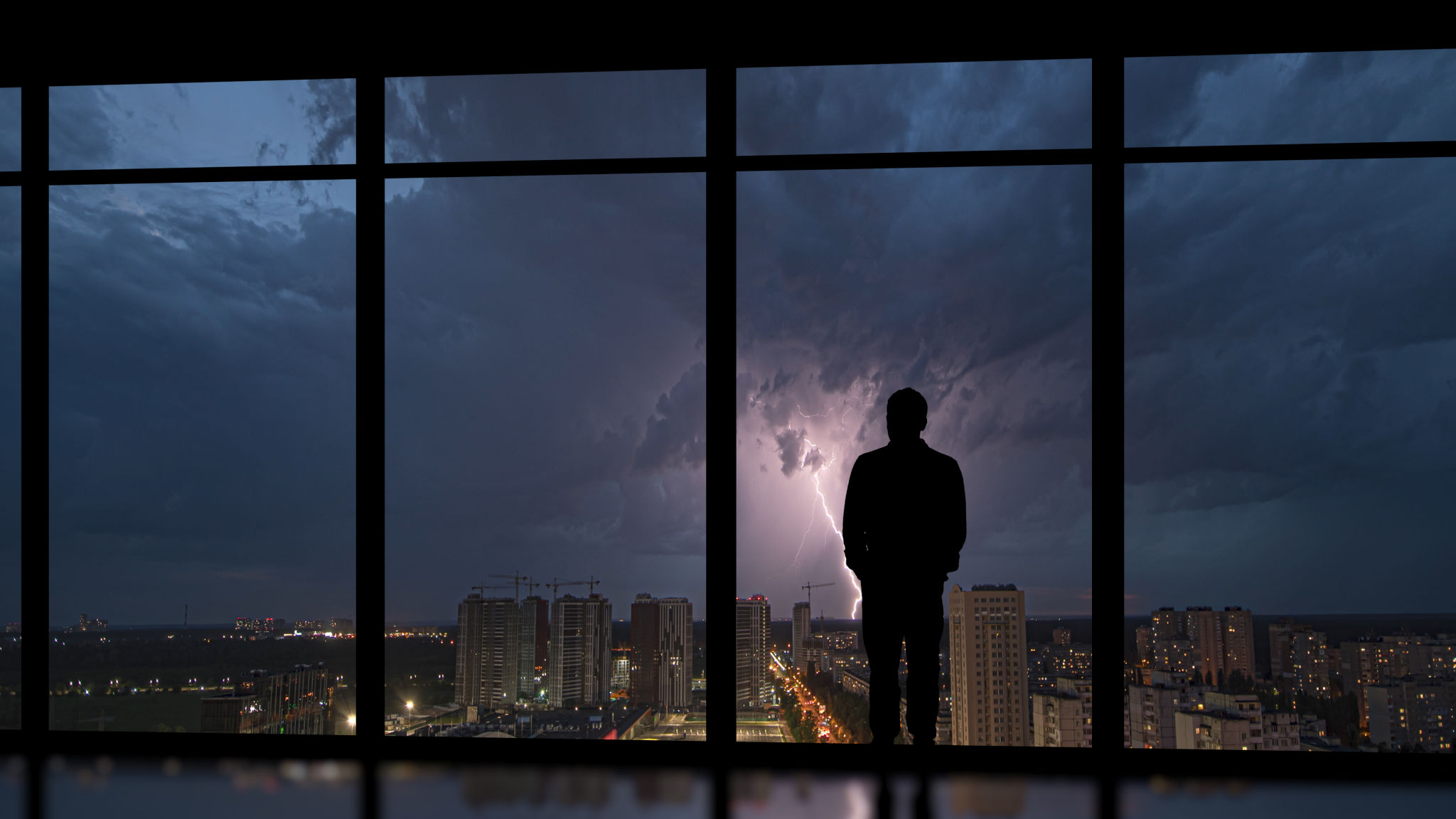 The man standing near the panoramic window on the night lightning background The man standing near the panoramic window on the night lightning background