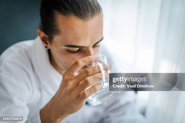 junger mann, der wasser aus einem glas trinkt. durst / einnahme von medikamentenkonzept. - fainted stock-fotos und bilder