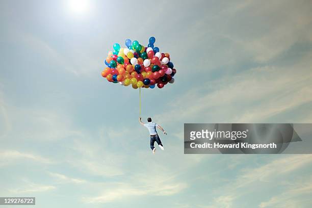 man lifted into sky by huge bunch of balloons - globo de helio fotografías e imágenes de stock