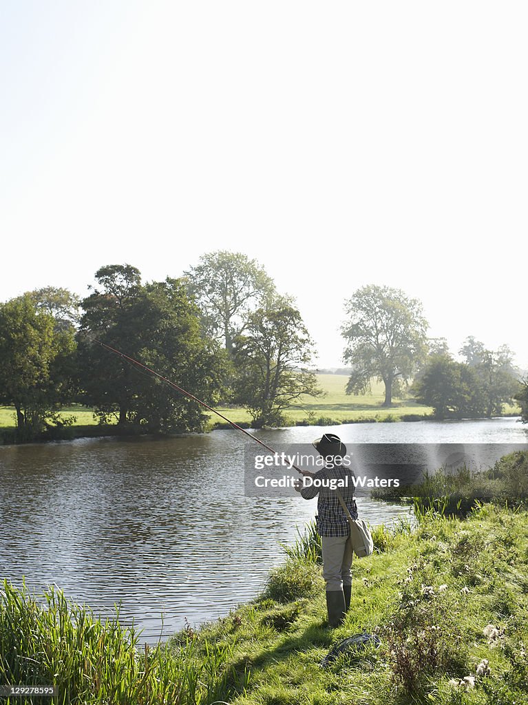 Man with fishing rod by lake.