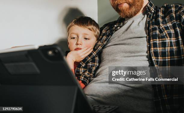 bored child sits beside a father and watches an electronic device screen - digital devices beside each other stockfoto's en -beelden