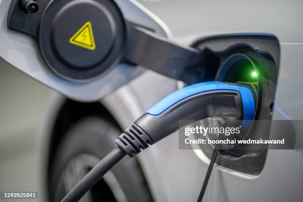 ev car or electric vehicle at charging station with the power cable supply plugged in on blurred nature with blue enegy power effect. - fahrzeug mit hybrid antrieb stock-fotos und bilder