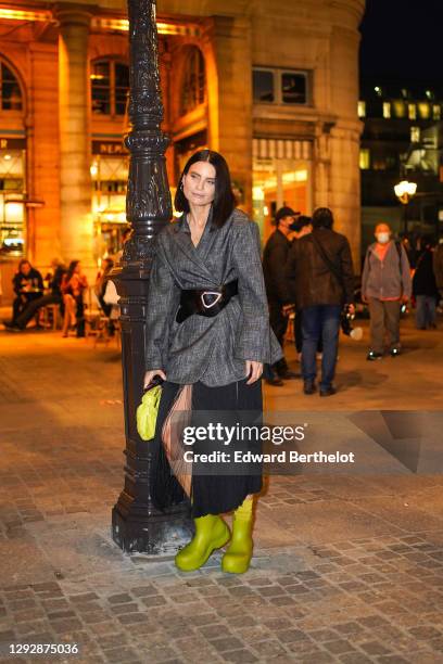 Guest wears a gray oversized blazer jacket, a large leather belt, a black pleated mesh skirt, a neon yellow woven leather bag from Bottega Veneta,...