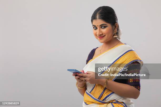 woman smiling while texting on her phone - kerala saree stock pictures, royalty-free photos & images