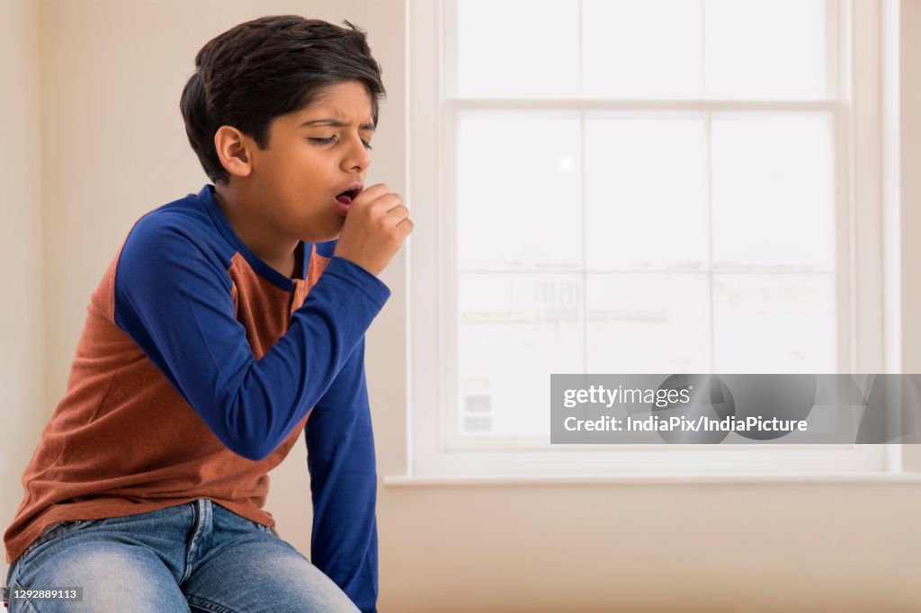 Portrait of a young boy coughing at home. (Children)