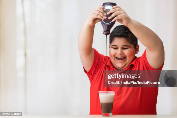 young boy filing the glass of milk with chocolate syrup.(obesity) - chocolate milk bottle stock pictures, royalty-free photos & images