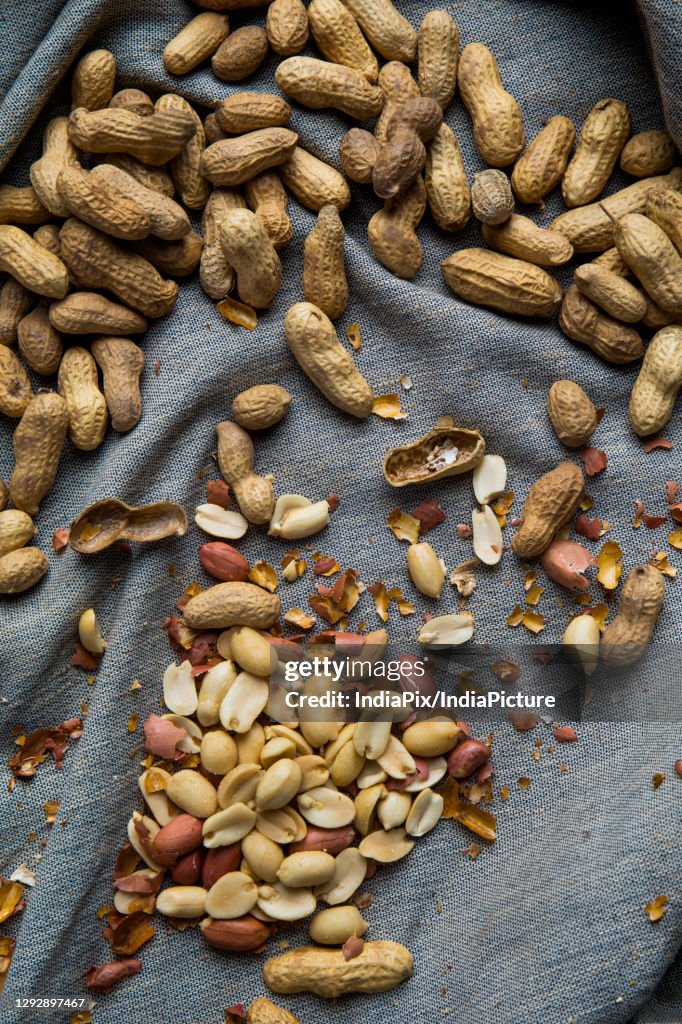 Raw groundnuts scattered on a grey cloth with peanut peels.
