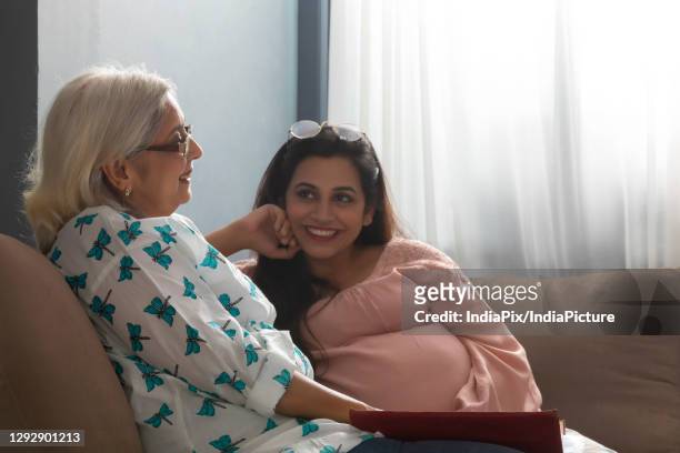 a pregnant woman looking lovingly at mother sitting besides on sofa - mother in law stock pictures, royalty-free photos & images