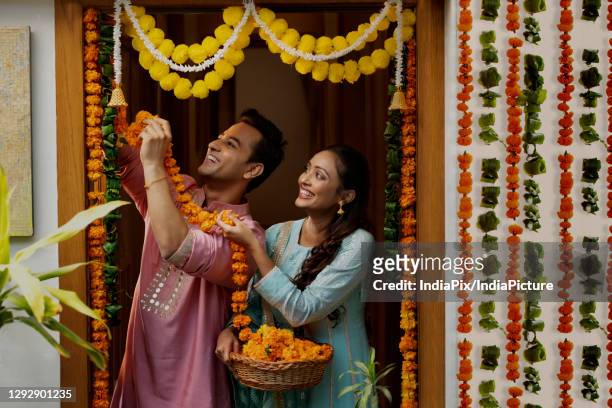 a husband happily hanging flower garlands with wife helping - decoration stock pictures, royalty-free photos & images